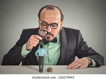 Curious Corporate Businessman Skeptically Meeting Looking At Small Employee Standing On Table Through Magnifying Glass Isolated Office Grey Wall Background. Human Face Expression, Attitude, Perception