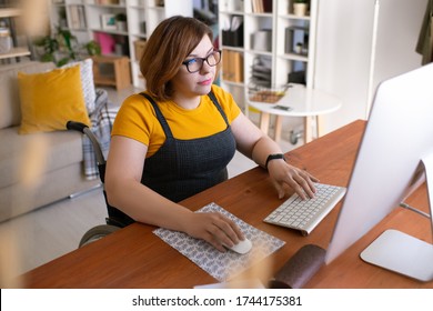 Curious disabled female student sitting in wheelchair and using computer while studying online
