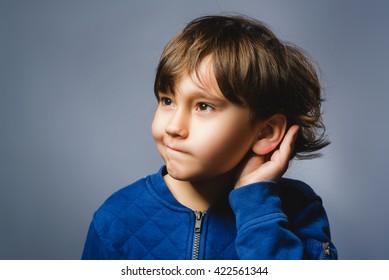 Curious Disappointed Boy Listens. Closeup Portrait Child Hearing Something, Parents Talk, Hand To Ear Gesture Isolated Grey Background. Human Face Expression, Emotion, Body Language, Life Perception