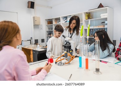 Curious elementary school students learning science, experimenting with colorful chemicals and using microscope with their teacher in laboratory class