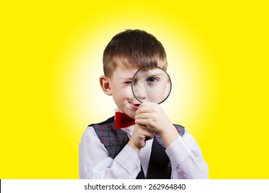 Curious Exploring little boy with magnifying glass, on yellow background.