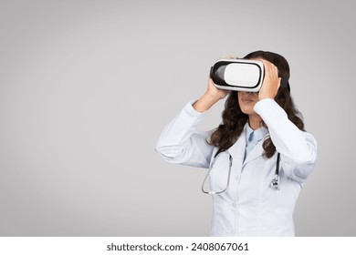 Curious female doctor experiencing virtual reality with VR headset, engaging with digital technology for medical training, grey background - Powered by Shutterstock