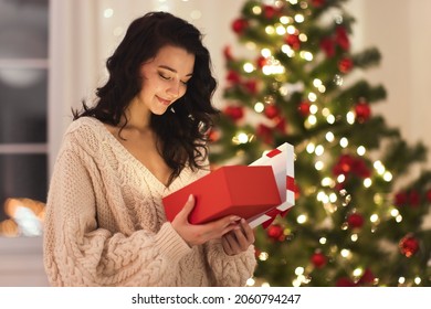 Curious happy romantic woman standing against Christmas tree background. Cheerful lady surprised of the present after the opening in the gift box. Marry Christmas and Happy Holidays - Powered by Shutterstock