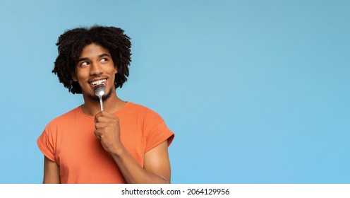 Curious and hungry young african american man with spoon in his mouth looking at copy space, dreaming about delicious healthy food, choosing something to eat, blue studio background, panorama - Shutterstock ID 2064129956