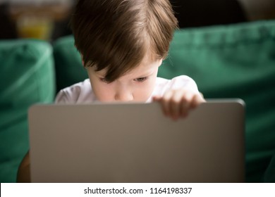 Curious interested kid boy secretly looking watching forbidden censored adult only internet online video content on laptop alone, parental protection, computer control and security for child concept