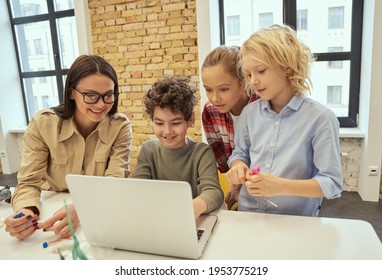 Curious Learners. Young Female Teacher In Glasses Showing Scientific Robotics Video To Joyful Children Using Laptop During STEM Class