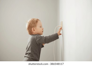 Curious Little Boy Playing With Electric Plug. Trying To Insert It Into The Electric Socket. Danger At Home