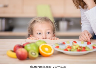 Curious little girl looking at cropped mother prepare fruit salad in the kitchen