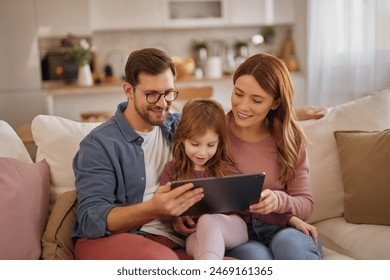 Curious little girl using the tablet with her parents in the living room - Powered by Shutterstock