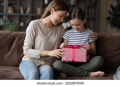 Curious little preteen kid girl unwrapping gift box, feeling excited getting present from caring mother, celebrating happy birthday. Smiling young mum congratulating small child daughter at home.