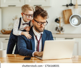 Curious Little Son Looking At Laptop Screen While Busy Dad In Formal Outfit With Messed Up Hair Working On Remote Business Project At Home
