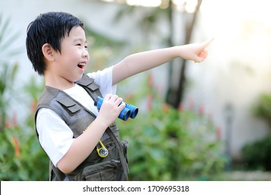 Curious little young Asian boy holding a binoculars and point finger out in the garden. Exploring the world, outdoors activity. Feeling fun. Boy wear green outdoors vest. Holiday, education concept  - Powered by Shutterstock