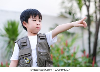 Curious little young Asian boy standing in the garden and point finger out. Exploring the world, outdoors activity. Feeling fun and happy. Boy wear green outdoors vest. Holiday, education concept  - Powered by Shutterstock