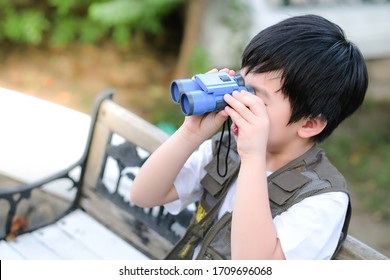 Curious little young Asian boy sitting on the chair and looking through a binoculars in the garden. Outdoors activity. Feeling fun and happy. Boy wear green outdoors vest.  Holiday, education concept  - Powered by Shutterstock