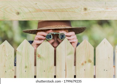 Curious neighbor stands behind a fence and watches with binoculars