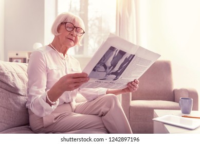 Curious Old Lady. Curious Old Lady Attentively Reading Newspaper Wearing Big Clear Glasses And Light Clothes