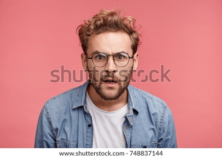 Curious scrupulous male model with trendy hairrdo and beard looks attentively at one point, sees something strange or suspicious. Angry man tries to overhear wife`s talk, looks annoyed, feels jealous