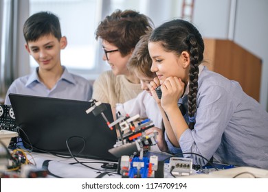 Curious smart caucasian pupils kids with female teacher enjoying science robotics lessons in technical school using laptop, study programming skill