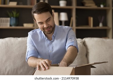 Curious Smiling Young Man Unpacking Carton Box, Getting Order From Internet Store. Joyful Male Client Satisfied With Fast International Delivery Service, Having Positive Online Shopping Experience.