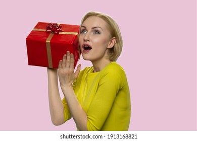 Curious surprised european lady with a gift box. Astonished adult woman isolated on pink background.