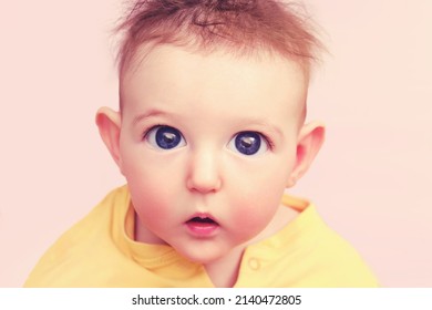 Curious Toddler Baby Boy With Big Eyes On A Pink Background, Face Close-up. Portrait Of A Confused Child With Disheveled Hair