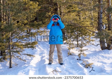 Curious traveler equipped with binoculars exploring the winter wilderness, surrounded by pine trees Birdwatching, zoology, ecology Research in nature, observation of animals Ornithology