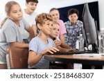 Curious underage boys and girls looking at monitor of computer together with trainer during IT courses