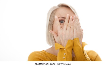 Curious woman covering face with hands peeping spying eye on white studio wall, funny woman feeling afraid fear shy hiding looking at camera through fingers isolated on light blank background - Shutterstock ID 1349905766