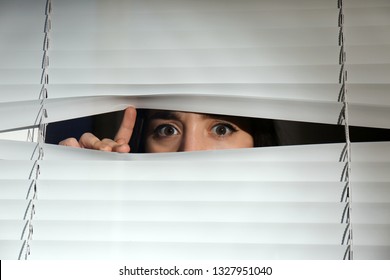 Curious woman looking through Venetian window blinds - Powered by Shutterstock