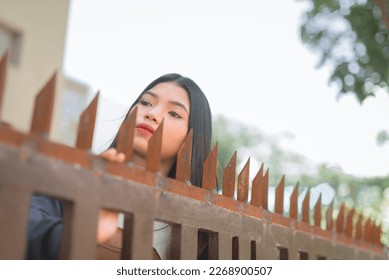 A curious woman peers over the fence to see the commotion across the street. Anxiously waiting for her partner to arrive. - Shutterstock ID 2268900507