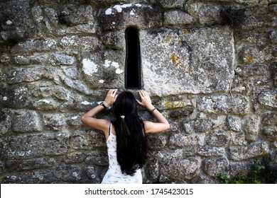 Curious Woman Trying To Climb A Stone Wall To Look Through A Window