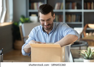 Curious young man in eyeglasses unpacking huge cardboard box, feeling excited of purchasing wished item in internet store. Happy millennial male customer satisfied with fast delivery service at home.