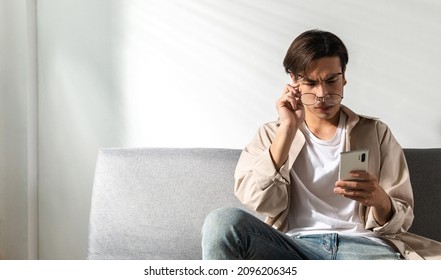 A Curious Young Man Looks At A Cellphone, Upset By Bad News, A Teenager Is Stunned He Is Taking The Glasses Off After Reading A Negative Bullying Message. A Trouble Online Issue Notification Concept.