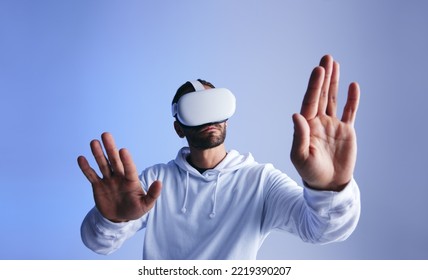 Curious young man touching virtual space with his hands. Young man experiencing a 3D simulation. Young man interacting with the metaverse using virtual reality goggles.