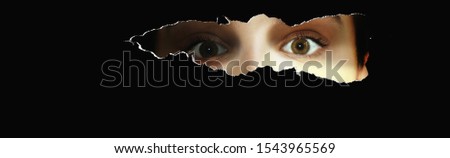 Curious young woman looks through a slit and looks terrified or amazed