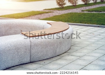 Curiously curved concrete bench with wooden slats for sitting in a city park in autumn