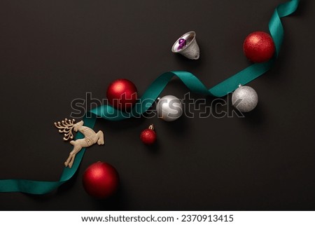 A curled ribbon in teal color decorated with a silver bell, a reindeer and several baubles. Black background. Christmas is a feast central to the Christian year