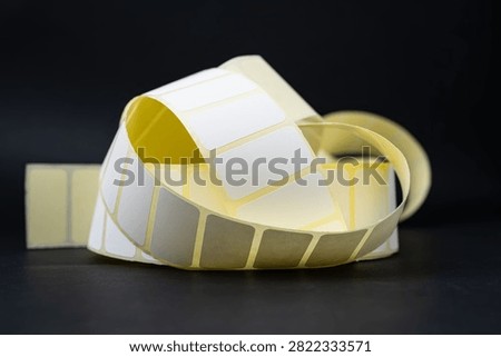 Curled roll of blank rectangular adhesive labels isolated on a black surface.