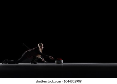 Curling player delivering a stone on a curling rink, sliding over the ice, isolated on the black background. Curling match curler athlete winter sports women.