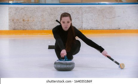 Curling training - a young woman with long hair on the ice rink holding a granite stone