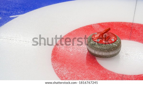 Curling, winter team olympic sport. Ice curling\
sheet with red and blue circle and visible pebbles. Ice rink and\
granite stone.