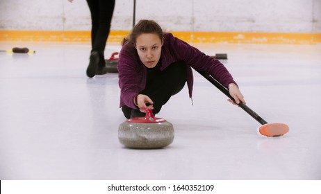 Curling - a woman skating on ice field with a granite stone holding a brush