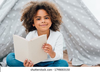 curly african american child holding book and looking at camera