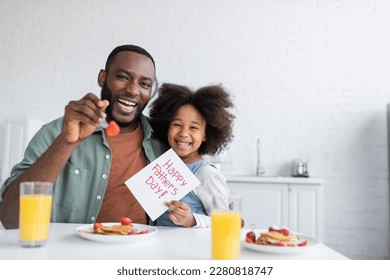 curly african american girl holding greeting card with happy fathers day lettering near cheerful dad during breakfast - Powered by Shutterstock