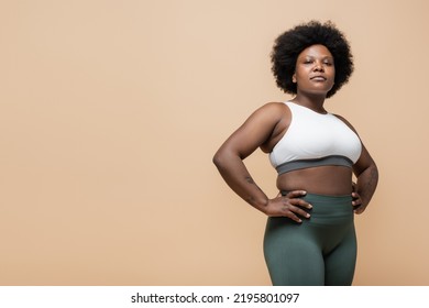 Curly African American Plus Size Woman In Crop Top Standing With Hands On Hips Isolated On Beige