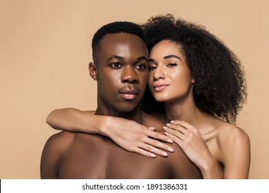 curly african american woman with bare shoulders hugging shirtless boyfriend isolated on beige