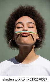 curly african american woman holding jelly straw with mouth while grimacing outside