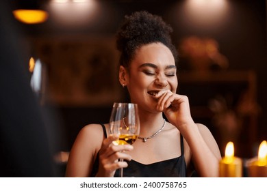 curly african american woman laughing and holding glass of wine during date on Valentines day - Powered by Shutterstock