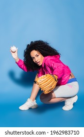 Curly African American Woman In Leather Glove Throwing Baseball On Blue