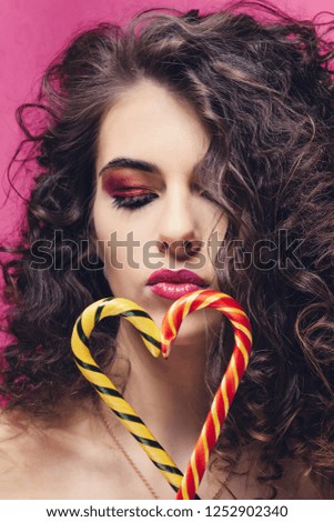 Curly beautiful girl with yellow and red lollipop sweet stick on pink background